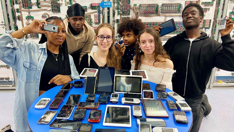 Young people surrounding a table with old mobile phones on