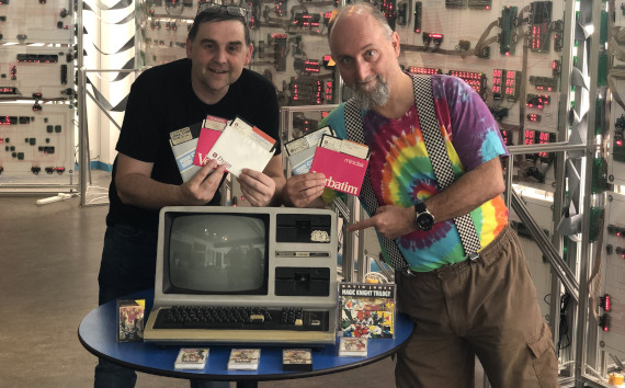 2 men holding documentation next to an old computer with a large processor in the background